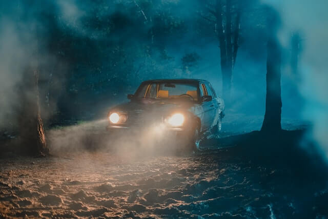 A car at night in the middle of a forest with its headlights turned on